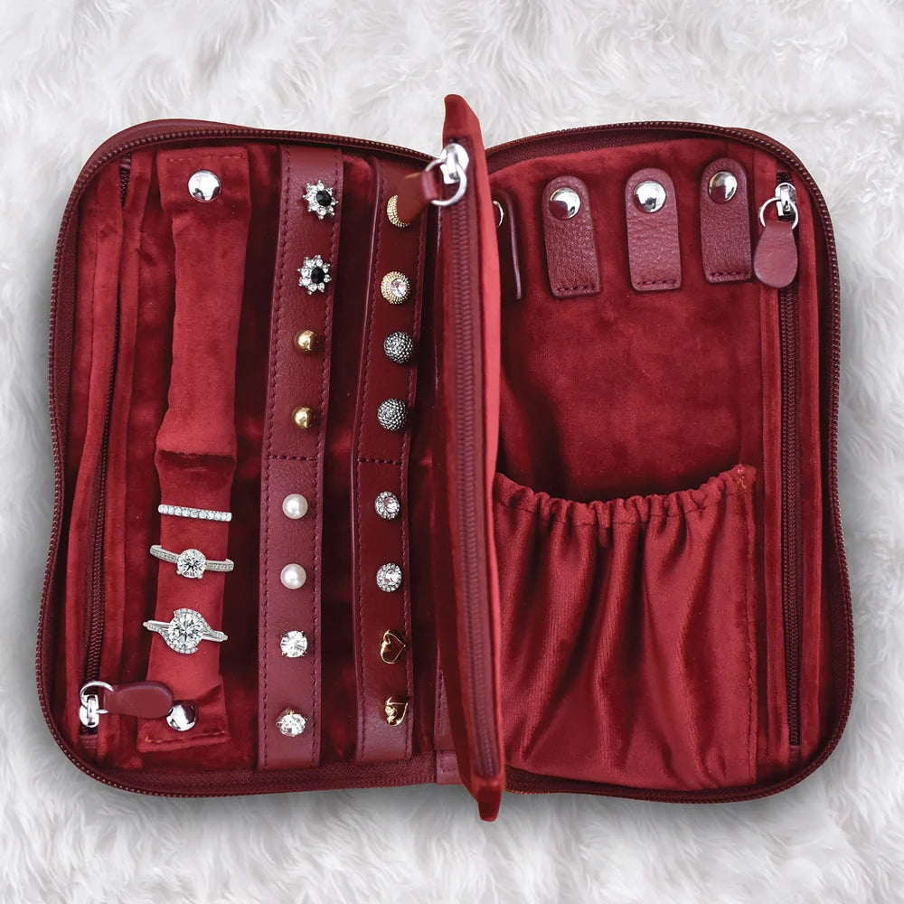 An open burgundy velvet jewelry organizer case with multiple compartments, ring slots, and pearl-like ring stands, shown on a white faux fur background.